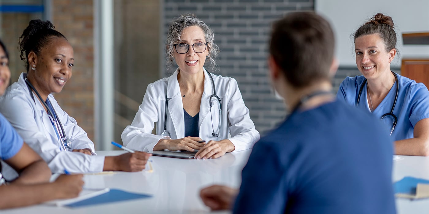 A diverse group of four medical professionals in scrubs, engaging in a meeting around a table.